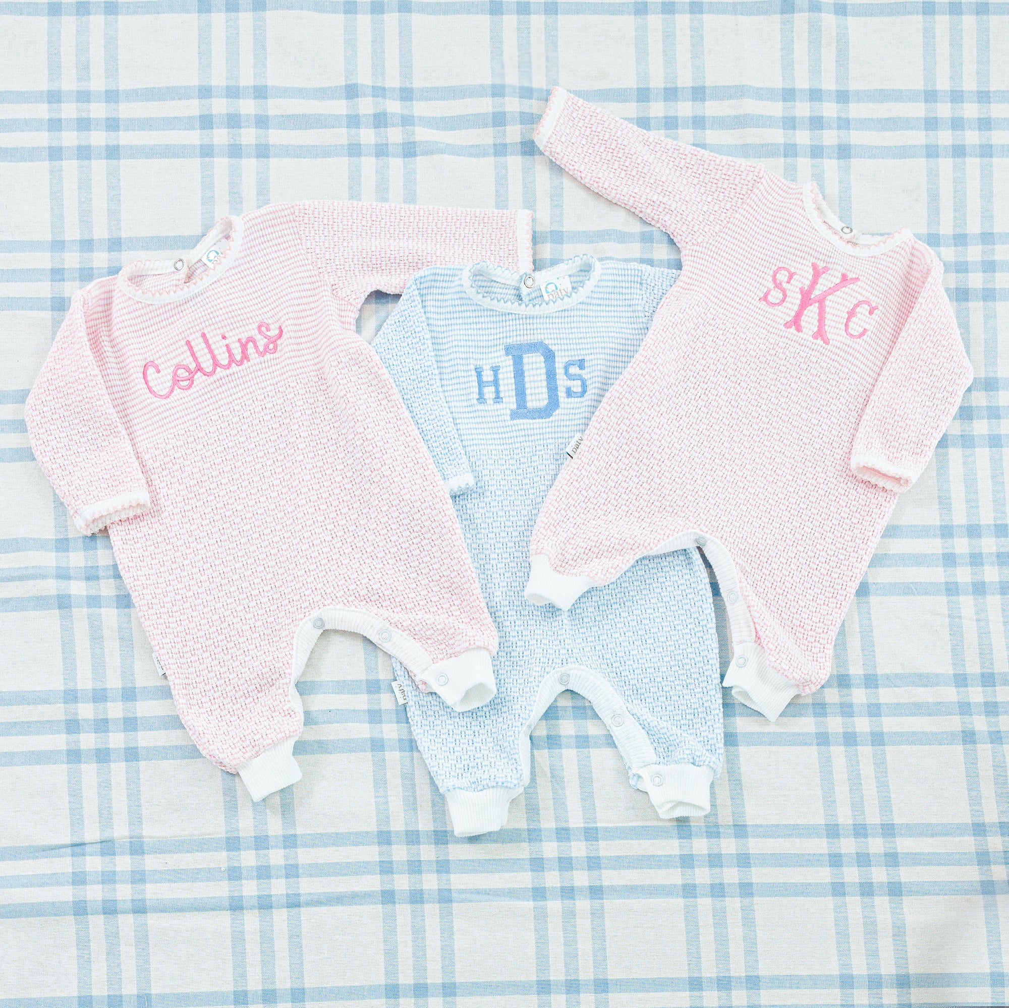 Two baby onesies, one in light blue and the other in light pink, both long-sleeved