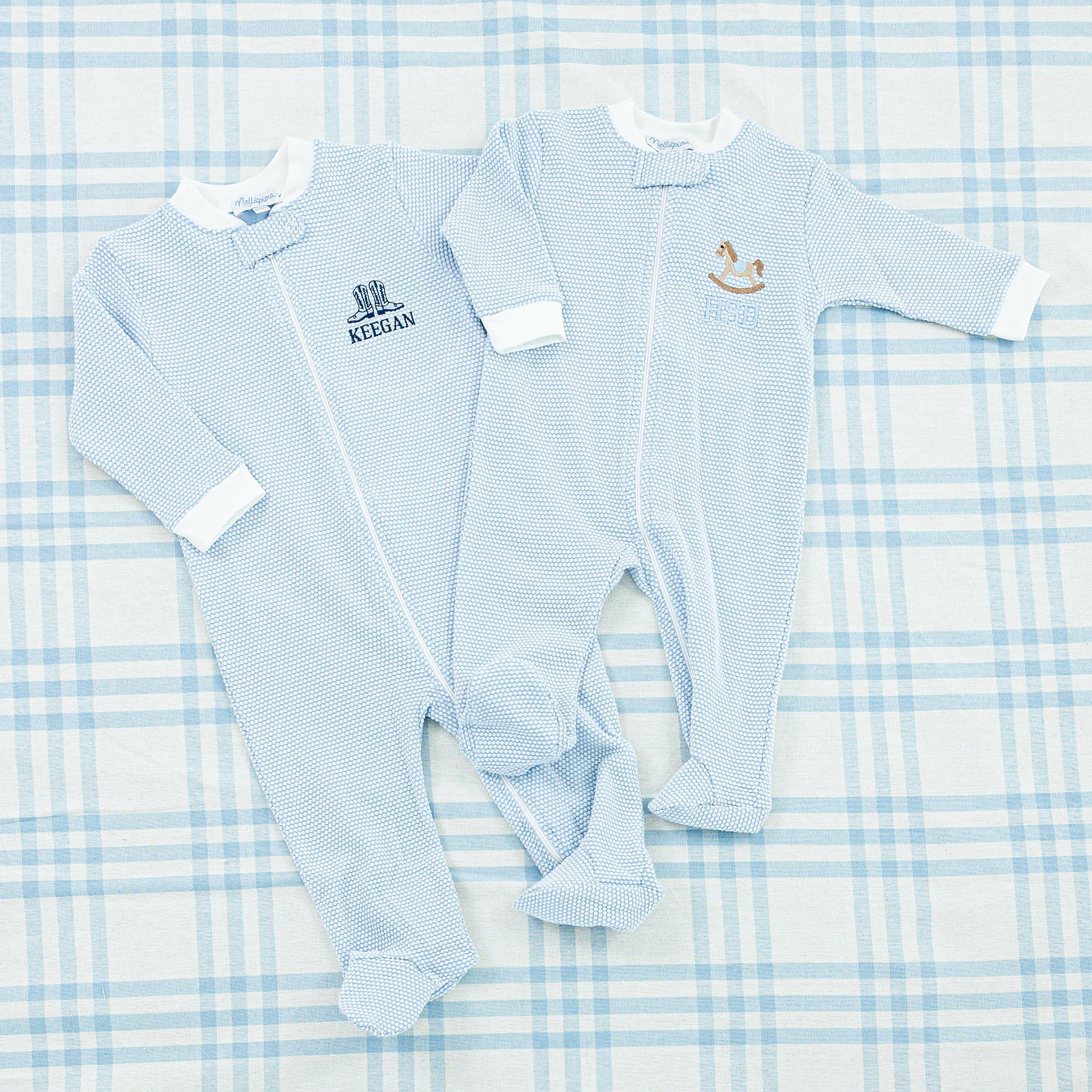 Two baby onesies, one in light blue and the other in soft pink with embroidered motif.