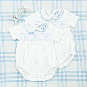 A close-up of two white baby onesies with light blue smocking and personalized monograms 