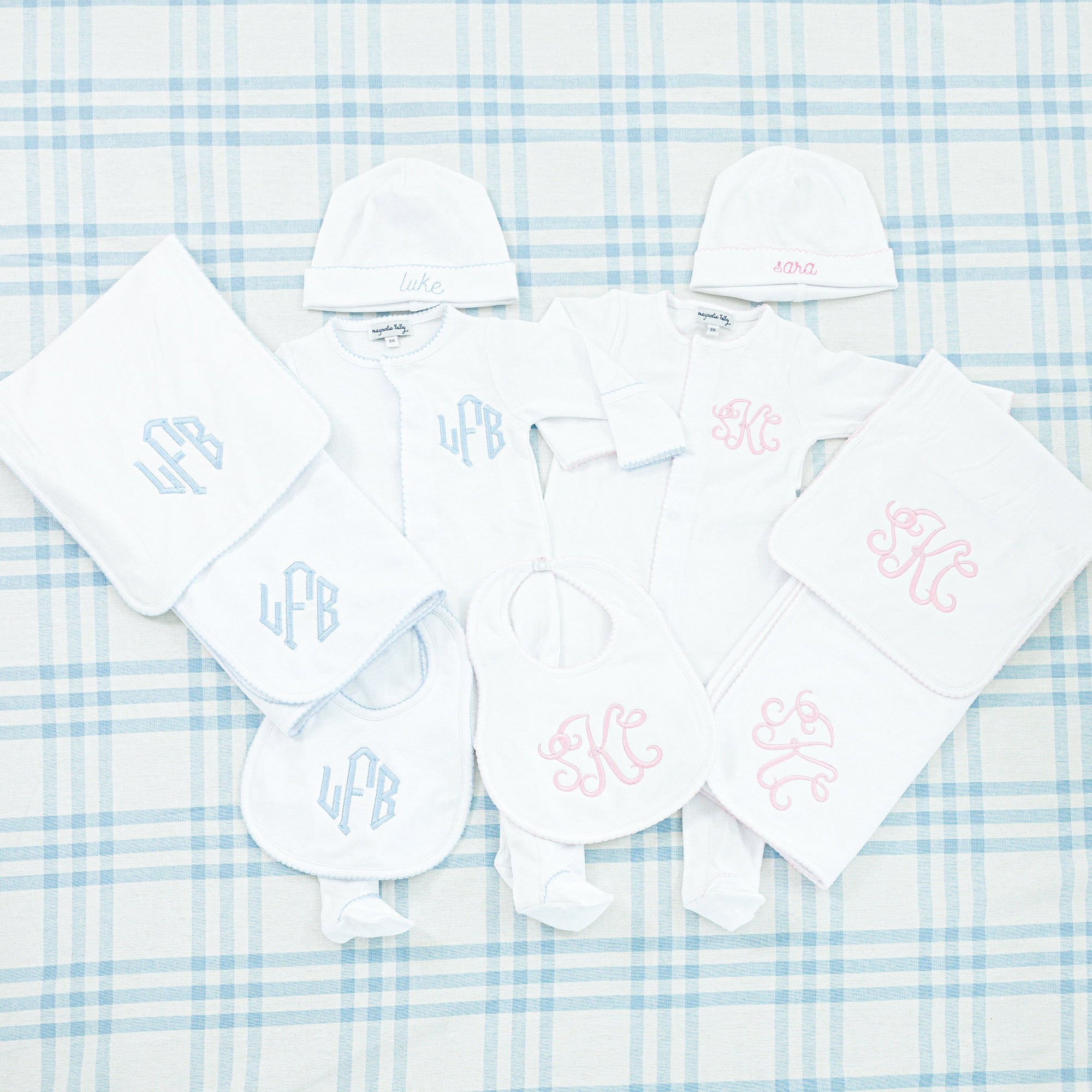 White baby gift set featuring a onesie, hat, bib, burp cloth, and blanket, all accented with pink trim