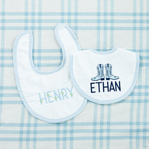 Two personalized baby bibs on a blue checkered fabric background