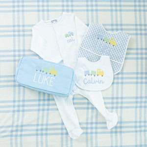 Personalized baby set featuring a white sleeper with blue train embroidery, matching bibs, and a blue pouch