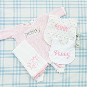 A personalized baby gift set featuring a pink gingham onesie with 'Penny' embroidered in a floral pattern