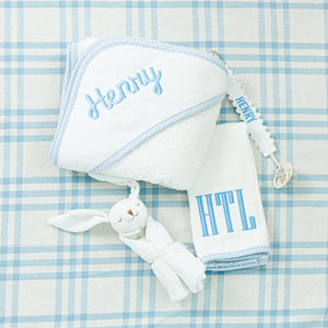 A personalized baby gift set: a hooded towel, matching washcloth, pacifier clip, and a soft bunny toy.