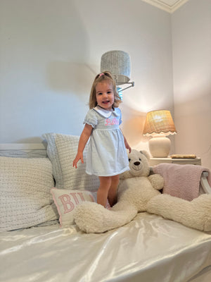 A young girl is wearing a light blue and white striped dress featuring a Peter Pan collar